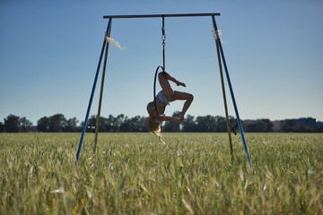 Young woman, blonde and athletic, with a body with flowers and pearls, performing exercises on a hoop suspended in the air, in a wheat field. Concept aerial hoop, yoga, gymnastics, pole dance, fitness © Manuel