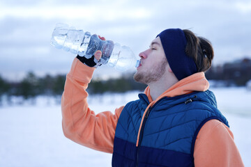 Young man, sportsman drink water after workout, training outdoors at winter cold day 