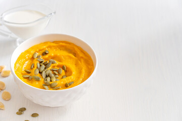 Homemade vegetarian healthy pumpkin soup made of pureed vegetables is a common Thanksgiving dish decorated with seeds served in bowl on white wooden background with copy space as traditional cuisine