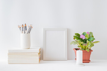 Mockup with a white frame, flowers in a pot on a light background. Empty poster frame mockup for...