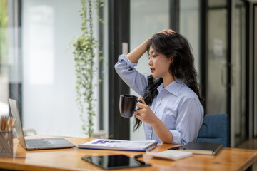 Young businesswoman takes a coffee break while working stressfully on a laptop in the office.