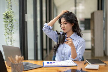 Young businesswoman takes a coffee break while working stressfully on a laptop in the office.