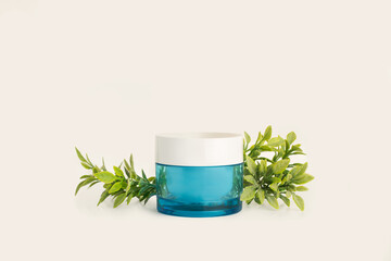 Bote de crema facial junto a unas ramitas y hojas verdes sobre un fondo blanco liso y aislado. Vista de frente y de cerca. Copy space