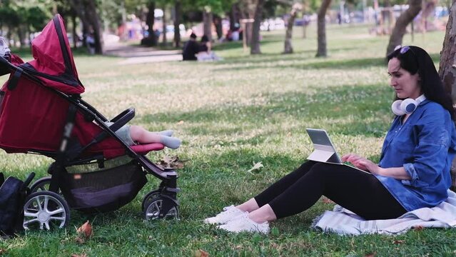 Cute feet in socks of little baby sleeping in buggy near mother working online via tablet computer in summer park healthy child sitting in carriage closeup