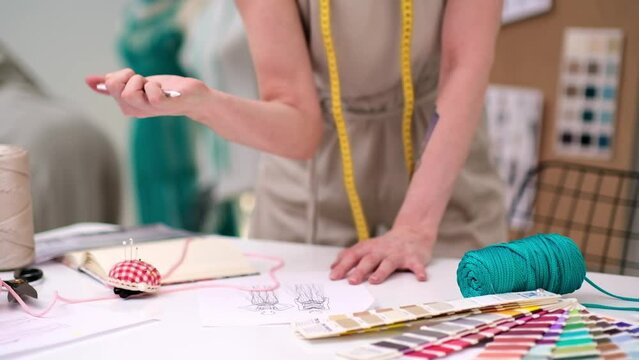 Woman fashion designer draws sketch holding green thread at desk in sewing atelier clothing dressmaker creates elegant outfit models working in tailor studio