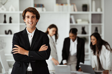 Happy european businessman in suit standing with folded arms in front of his colleagues, posing in office during meeting