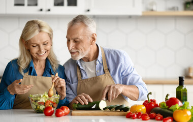 Happy senior couple preparing healthy salad together in kitchen interior