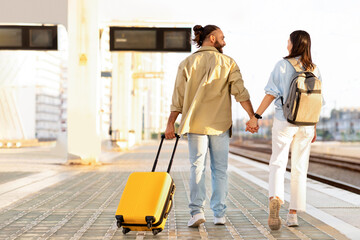 Happy millennial caucasian couple with suitcase hold hands, go to transport on train station, back,...