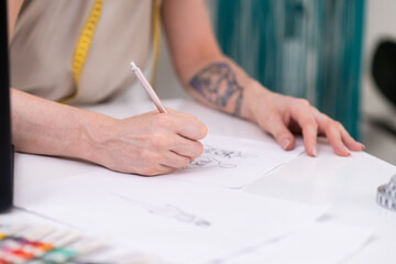 Woman draws dress model sitting at desk in clothes atelier talented designer makes sketch of stylish apparel for women in fashion studio closeup sewing industry
