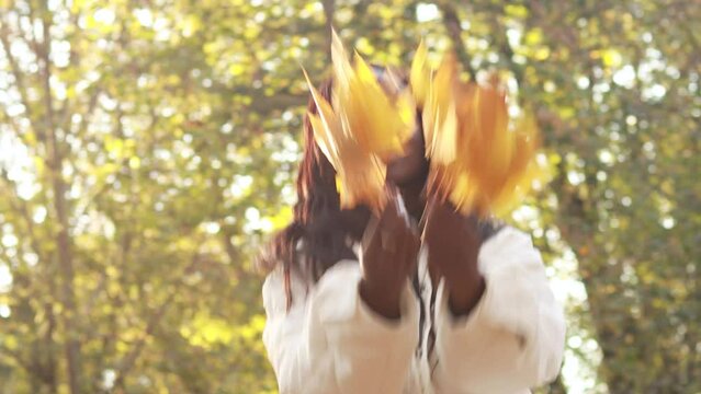 4k footage. African american woman dancing with small bouquets of yellow orange red leaves hold in hands, portrait of young latin lady in warm sunny autumn park season, fall
