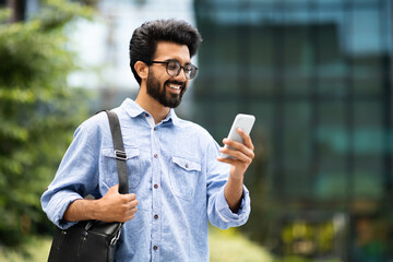 Cheerful indian guy going to office, using cell phone