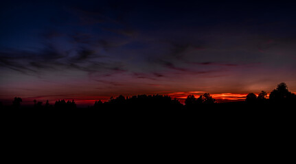Naklejka premium Dark silhouette of leaf trees after cloudy red sunset in Krkonose mountains