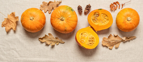 Obraz na płótnie Canvas Fresh pumpkins with autumn leaves on a beige textile background. Top view, flat lay, banner.