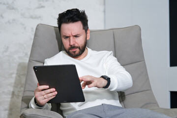 Man is using tablet computer at home sitting in armchair