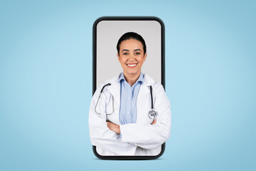 Young brazilian woman doctor in white uniform posing with folded arms in huge cellphone screen, blue background, banner