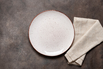 Empty white plate with a beige linen napkin on a brown rustic background. Top view, flat lay, copy space. - obrazy, fototapety, plakaty