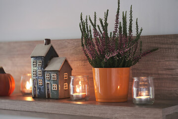 Autumn hygge home decor on shelf in the living room. Decorative house, candles, heather and pumpkin.