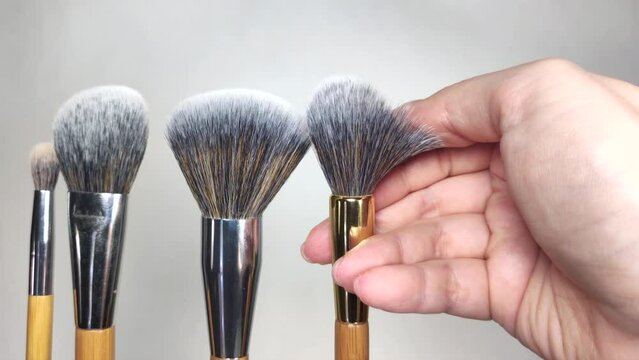 woman runs her hand through the bristles of a makeup brush, slow-motion shot macro