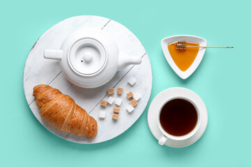 Wooden board with teapot, croissant, honey and cup of tea on color background