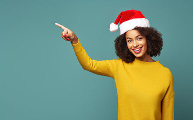 Fototapeta na wymiar Young black woman wearing a santa hat smiles with a joyful and shocked expression and points to the right.Generative AI