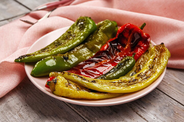 Plate with grilled chili peppers on grey wooden background