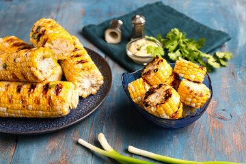 Plate and bowl of tasty grilled corn cobs with parsley on blue wooden background