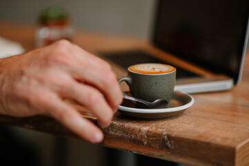 Man's hand lifting up a coffee spoon from the tray with a full cup of coffee.