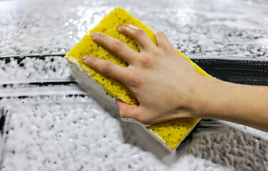 Close-up of hand cleaning black car of serviceman. The process of washing cars with foam and sponge. The man using yellow sponge to wash his car.