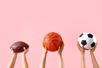 Female hands holding different sports balls on pink background