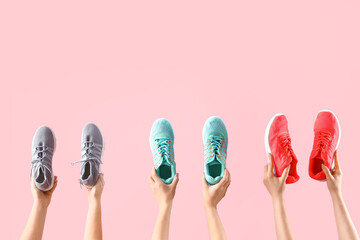 Female hands holding different sneakers on pink background