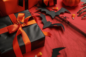 Composition with gift box, tasty candy corns and paper bats for Halloween on red background, closeup