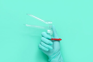 Hand in medical glove and with gynecological speculum on turquoise background