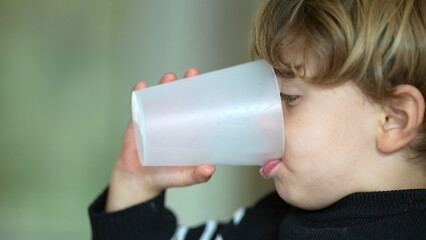 Little boy drinking water with plastic cup, profile close-up face of a caucasian male child sipping water, hydration and healthy lifestyle concept