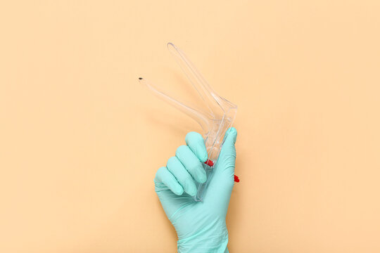 Hand in medical glove and with gynecological speculum on color background