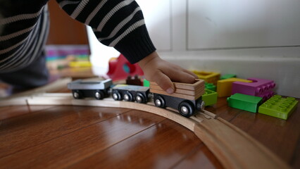 Little boy playing with vintage wooden train tracks, child immersed in imaginative play pushing...
