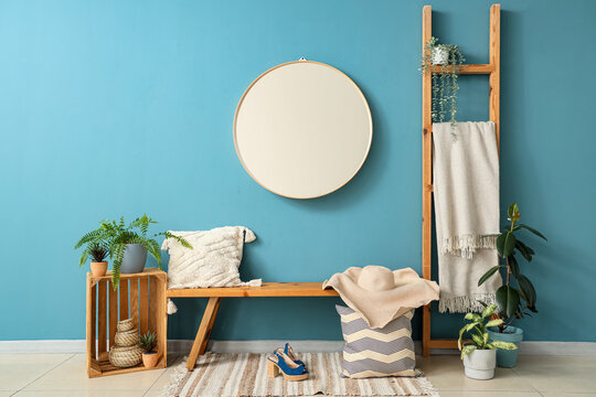 Wooden bench with pillows, female accessories and mirror near blue wall in hall