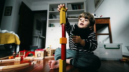 Little boy building a tower block, putting vintage blocks on top of one another, kid immersed in...