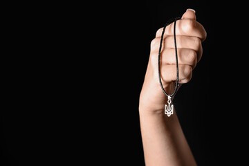 Female hand with Ukrainian trident pendant on dark background