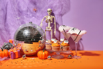 Halloween party composition with cupcakes, disco ball, drinks and decorations on orange table...