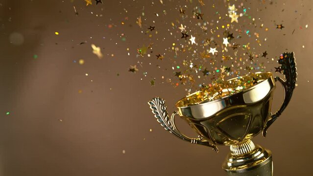 Super Slow Motion. Champion Golden Trophy with Exploding Gold Glitters and Stars against black background. Concept of Success, Victory or Achievement.