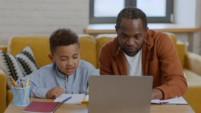 Cute little black boy studying online at home with his daddy, enjoying well done homework, tracking shot, slow motion