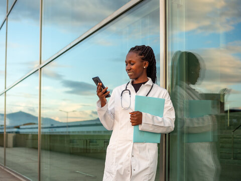 Young female doctor checking and typing on her phone in front of a hospital