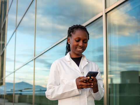 Young female doctor checking and typing on her phone in front of a hospital