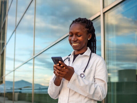 young female doctor typing on her phone outdoors in front of a hospital