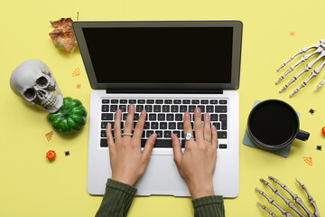 Female hands with laptop, cup of coffee and Halloween decorations on yellow background