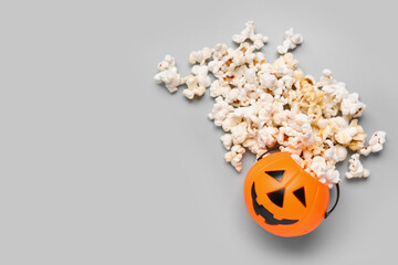 Bowl made of pumpkin with tasty popcorn for Halloween celebration on grey background