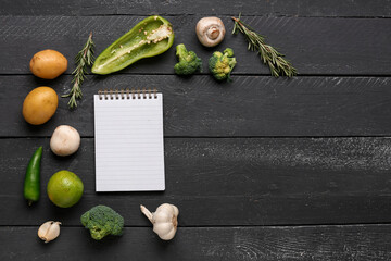 Blank notebook with fresh vegetables on black wooden table