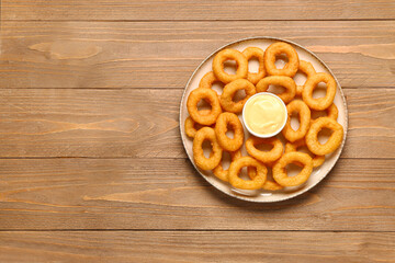 Plate with fried breaded onion rings and mayonnaise on wooden background