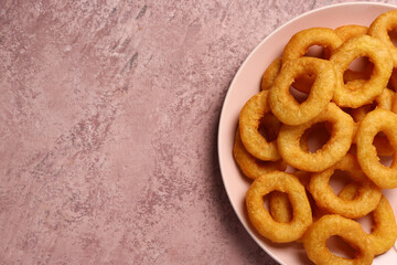 Plate with fried breaded onion rings on pink background