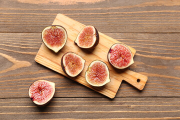Board with halves of fresh ripe figs on wooden background